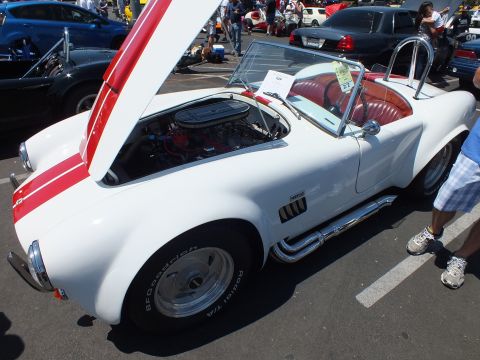 White Cobra-style roadster with hood open showing engine, red interior, at a car show