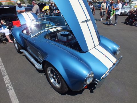 Blue Cobra-style roadster with white stripes, hood up showing chrome air cleaner