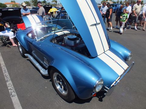 Rear three-quarter view of a blue white-striped Cobra-style roadster with hood open