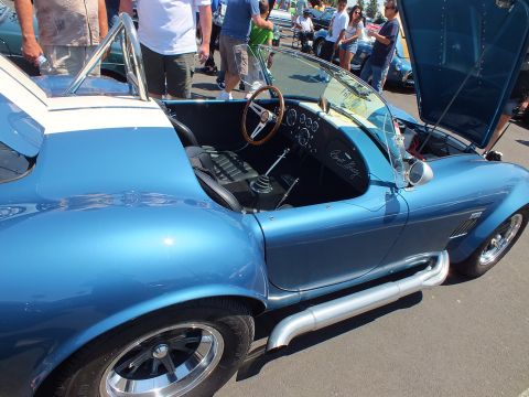 Side view of a blue Cobra-style roadster with wood steering wheel and chrome side pipe
