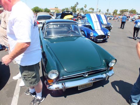 Front view of a dark green Sunbeam Tiger coupe with yellow California plate at a car show