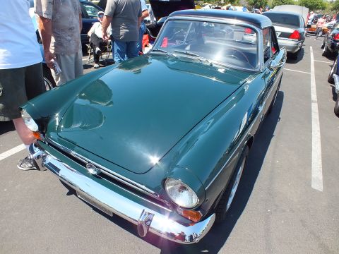 Front three-quarter view of a dark green sports coupe with chrome bumper at a car show