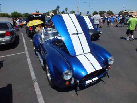 Front view of a blue Cobra-style roadster with white stripes at a busy car show