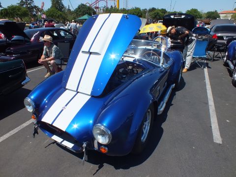 Blue white-striped Cobra-style roadster with hood up, amusement-park ride behind