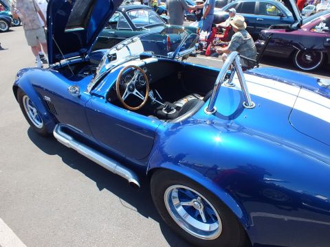 Side view of a blue white-striped Cobra-style roadster with wood wheel and chrome side pipe