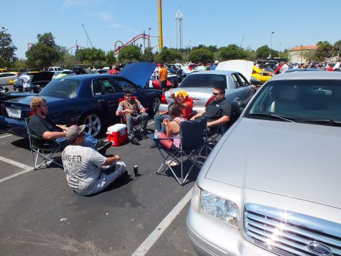 Car-show attendees seated in camp chairs with a roller coaster in the background