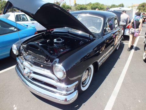 Black vintage Ford sedan front three-quarter with hood open at a show