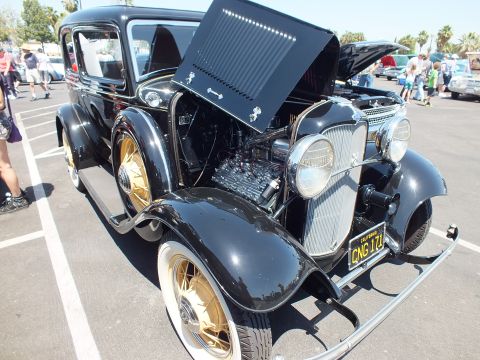 Front three-quarter of a black 1932 Ford sedan with gold wheels, hood up