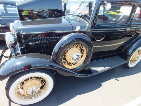 Side view of a black prewar Ford sedan with gold wire wheels