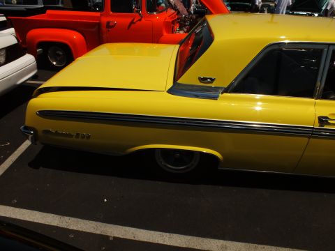 Side rear of a yellow Ford hardtop with red pickup in background
