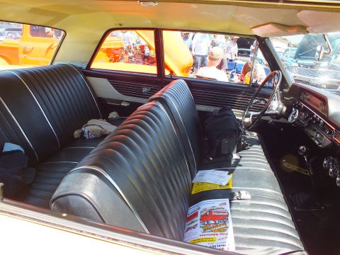 Black pleated front bench seat and dashboard interior of a vintage car at an outdoor show