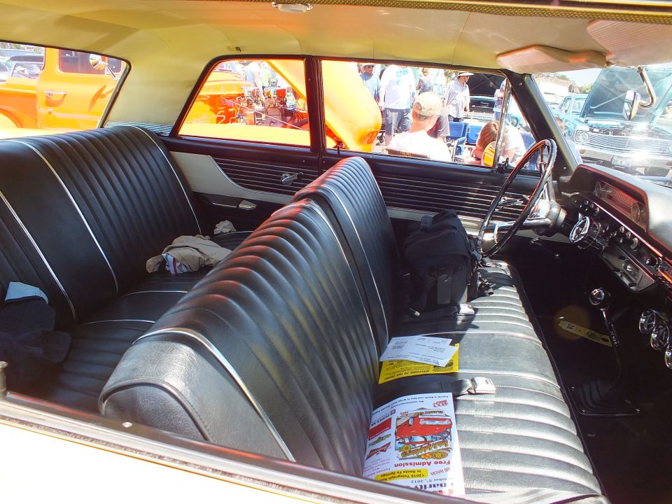 Black pleated front bench seat and dashboard interior of a vintage car at an outdoor show