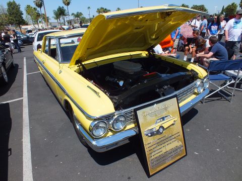 Yellow vintage station wagon with open hood at an outdoor car show