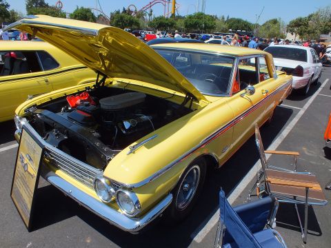 Yellow vintage two-door car with open hood at an outdoor car show