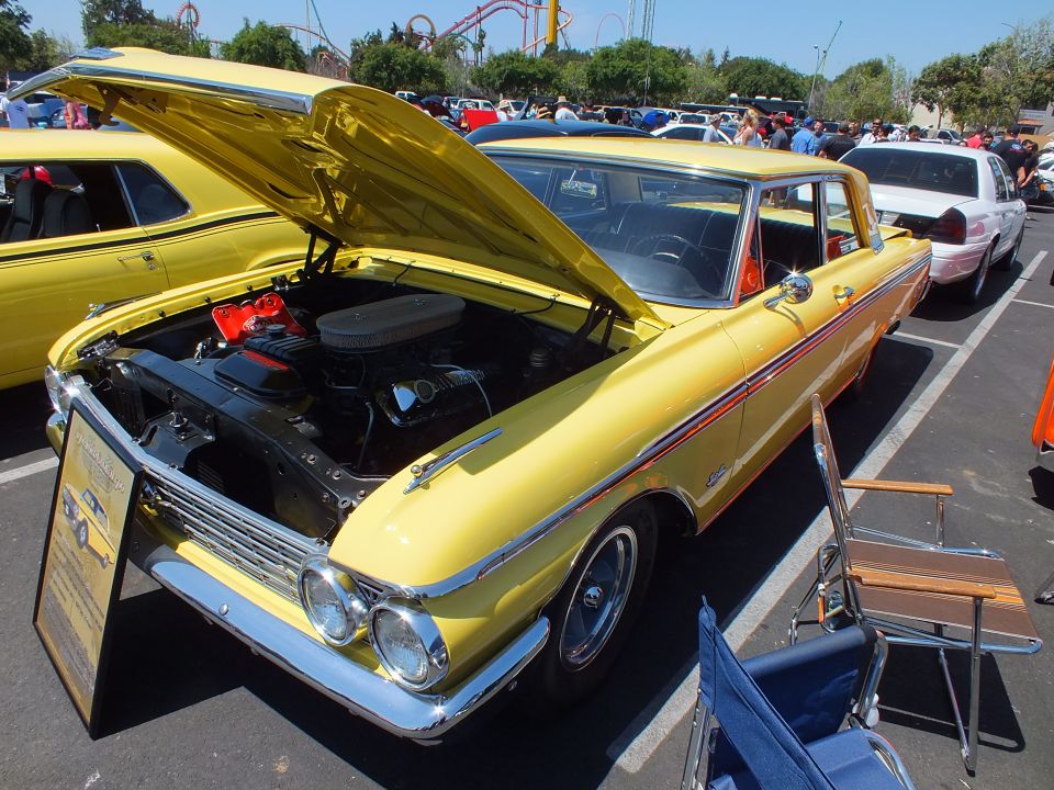 Yellow vintage two-door car with open hood at an outdoor car show