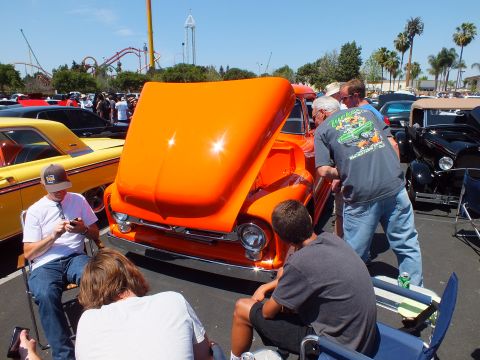 Orange classic pickup truck with open hood surrounded by spectators
