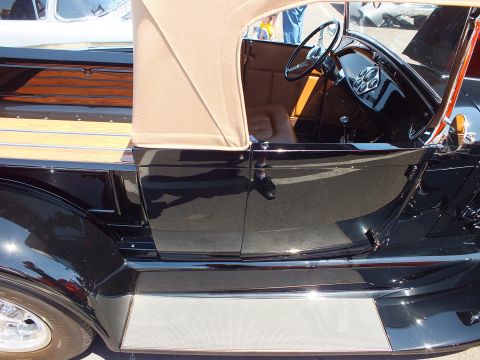 Black classic car with wood paneling and tan top, side view of interior