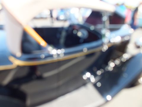 Heavily blurred out-of-focus image of a dark roadster indoors