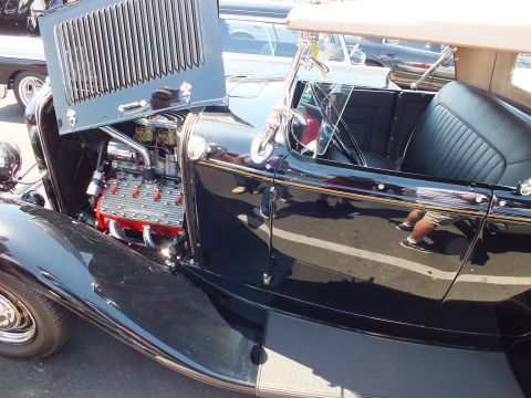 Black hot rod roadster with open hood showing chromed flathead V8 engine