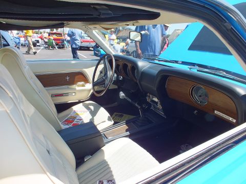 White interior of a Mustang with running-horse emblem on woodgrain dash