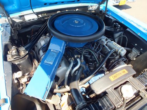 Top view of a blue V8 engine with black round air cleaner and caution-fan decal