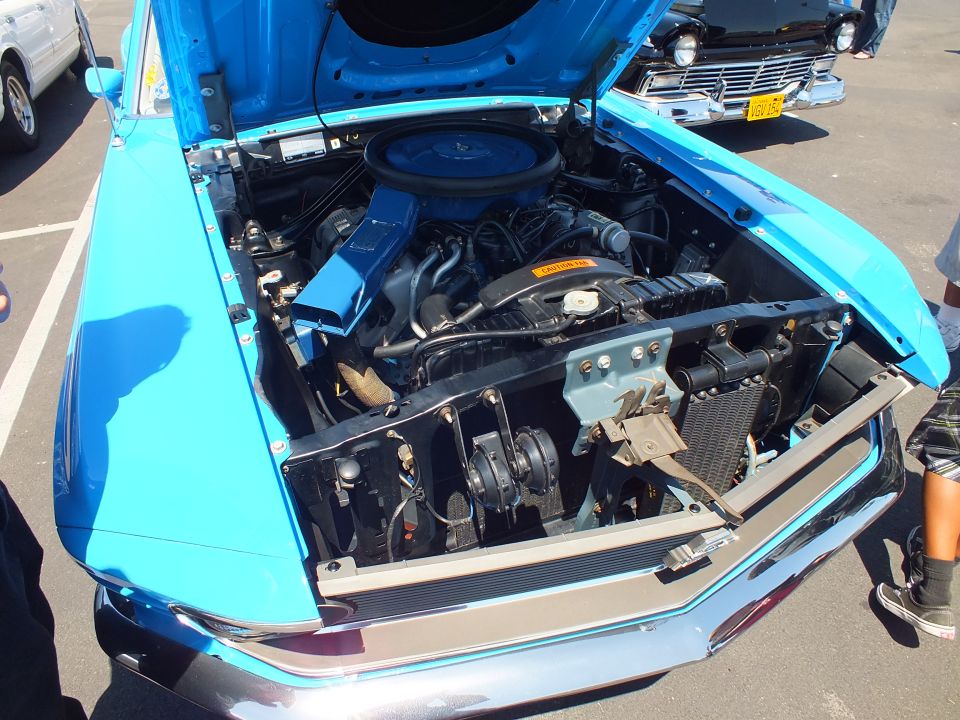 Front engine bay of a light blue Mustang with hood up at a car show