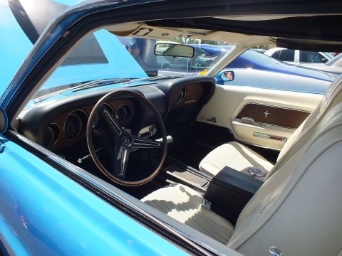 Interior of a Mustang with three-spoke wheel, woodgrain dash and white seats
