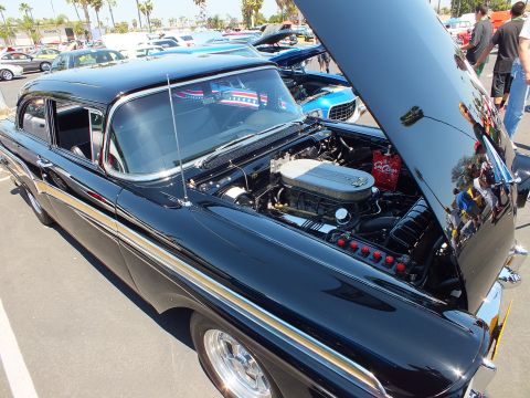 Black 1950s sedan with hood up showing chromed V8 at a car show