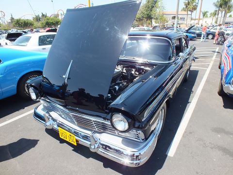 Black 1957 Ford sedan with hood up, front three-quarter view at a car show