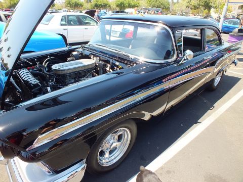 Black 1957 Ford two-door with pinstriping and open hood at a car show