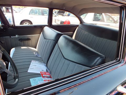 Black and gray cloth bench-seat interior of a 1950s car with show flyer
