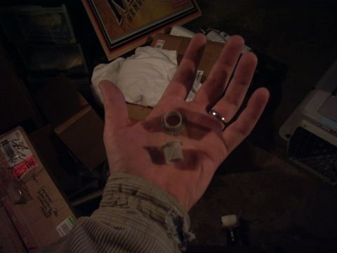 1991 Ford LTD Crown Victoria - A hand holds two small plastic parts, possibly bushings, with boxes and a white cloth in the background.
