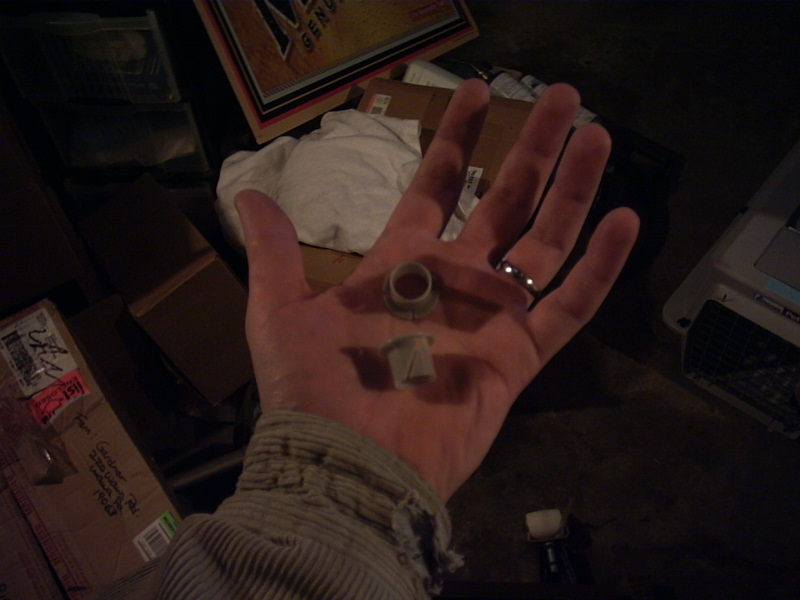 Hand holding two small plastic bushings. Boxes and a white cloth are in the background