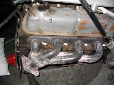 1988 Ford Bronco - Close-up view of an engine's exhaust manifold and spark plugs, with a portion of the valve cover visible.