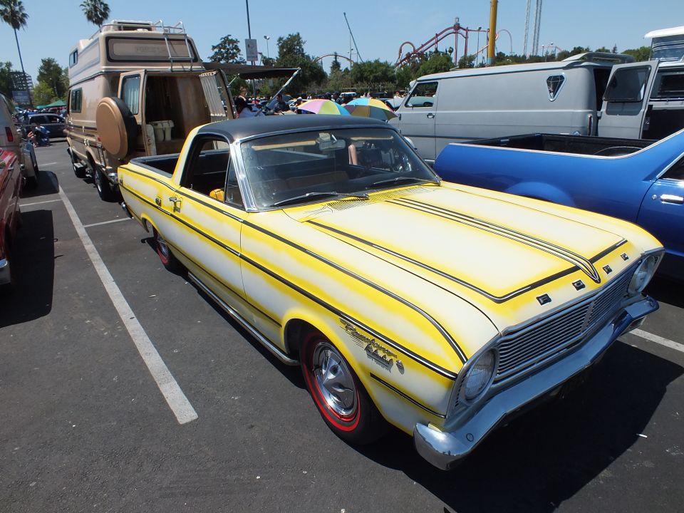 Yellow Ford Ranchero coupe-utility with black stripes towing setup at a show