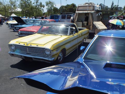Yellow Ford Falcon coupe-utility beside a blue car hood at a car show