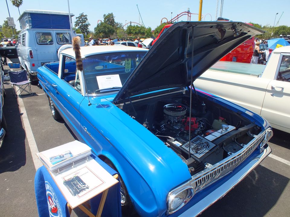 Blue 1960s Ford Ranchero pickup with raised hood and chrome V8 engine at a car show