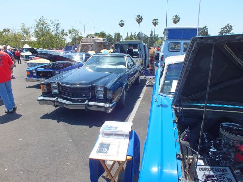 Car-show row with a black 1970s sedan and a blue pickup with open hood