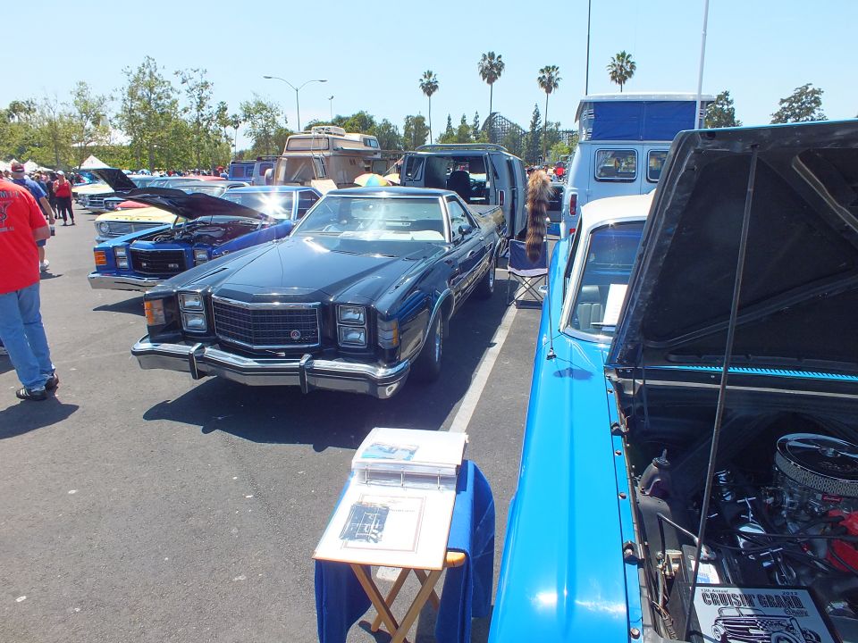 Car-show row with a black 1970s sedan and a blue pickup with open hood