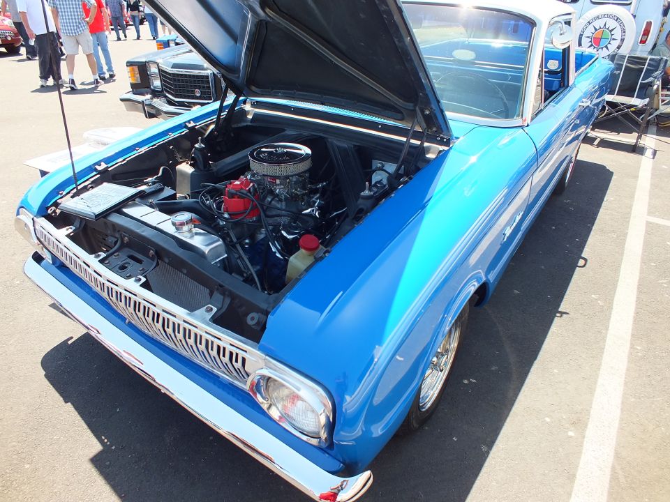 Blue early-1960s Ford with raised hood showing chrome V8 engine, three-quarter front view