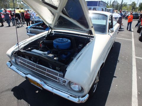 White early-1960s Ford Falcon with raised hood showing blue six-cylinder engine
