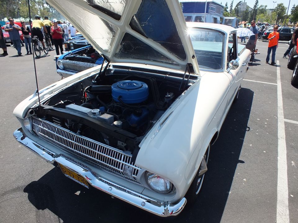 White early-1960s Ford Falcon with raised hood showing blue six-cylinder engine