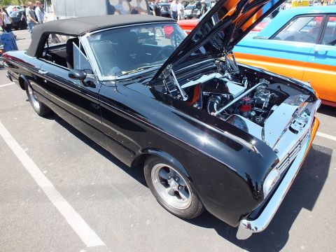 Black 1960s Ford Falcon convertible with black top and open hood at a car show