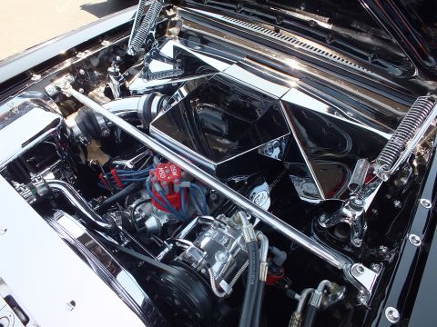 Close-up of a chromed custom engine bay with red plug wires and finned components