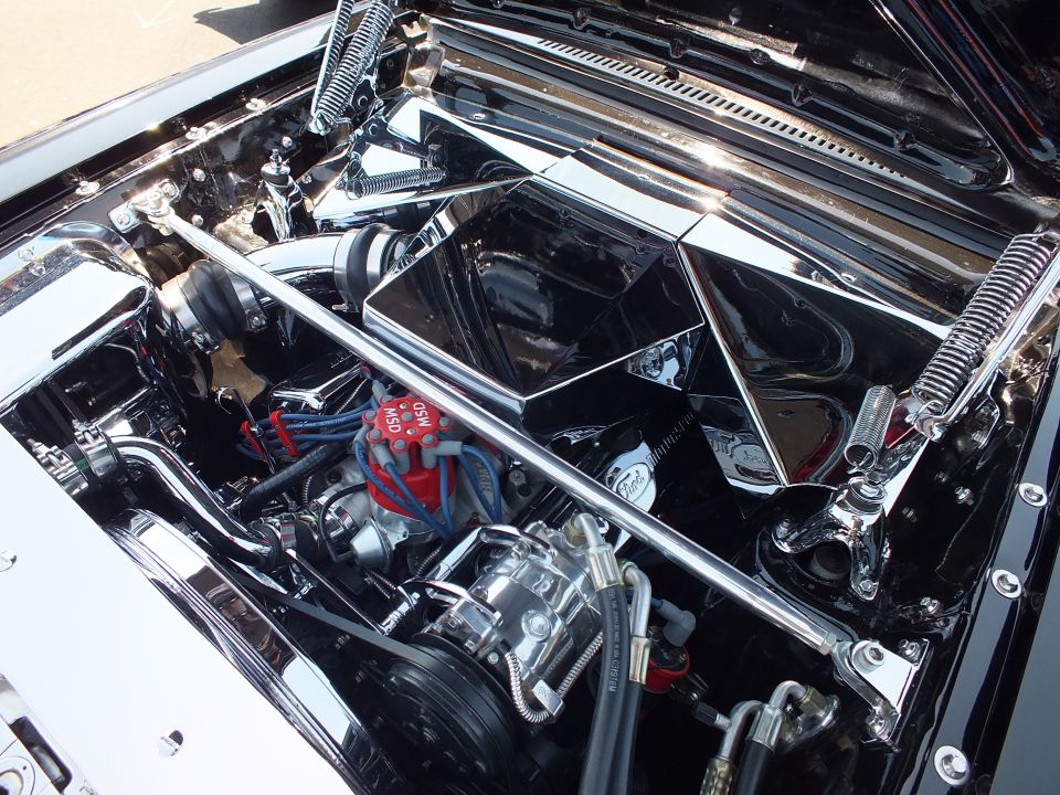 Close-up of a chromed custom engine bay with red plug wires and finned components