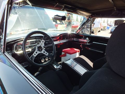 Black-trimmed interior of a custom classic car with deep-red dash and black seats