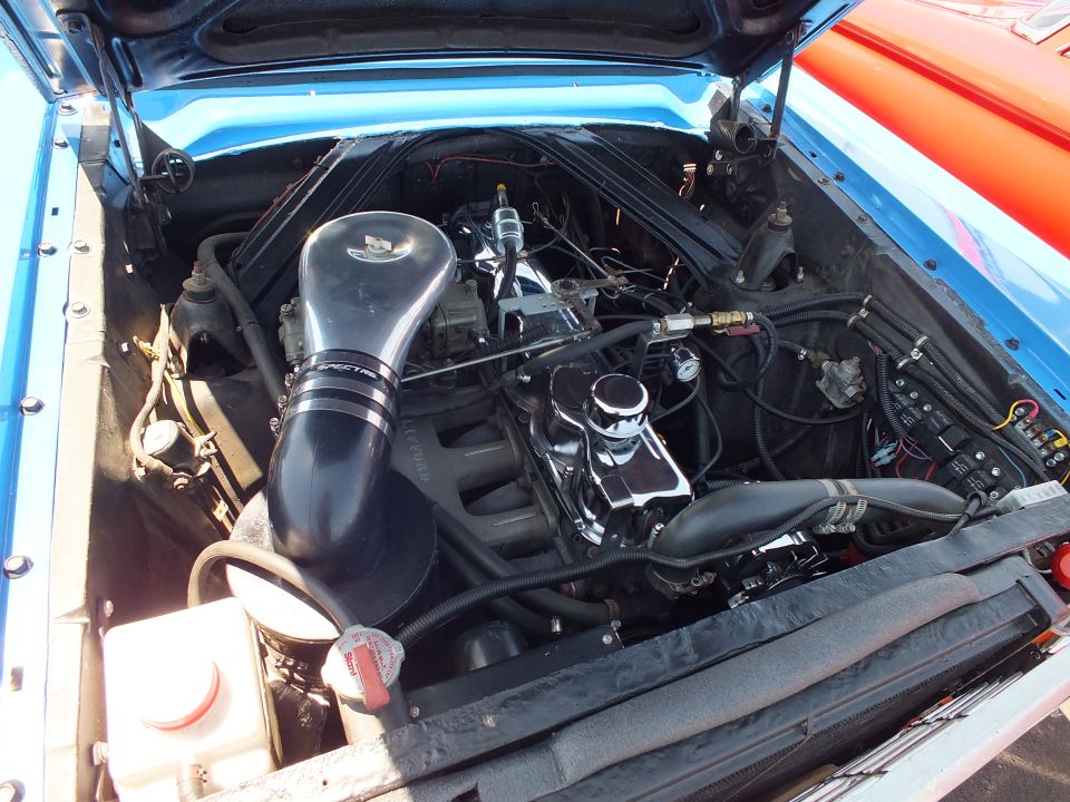 Engine bay of a blue Ford with black cold-air intake and finned valve covers