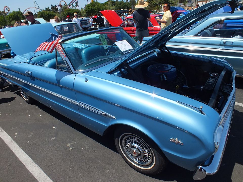 Light blue convertible with US flag and hood open at a car show