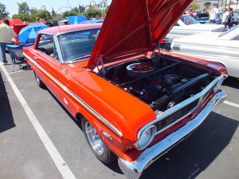 Orange-red classic coupe with hood open and chrome wheels at a car show