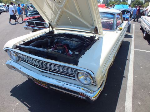Cream classic Ford with hood up and yellow plate at a car show